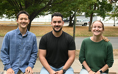 (L-R) Thomas Lee, Laurențiu Anton, and Rosie Keller sitting on a cement wall