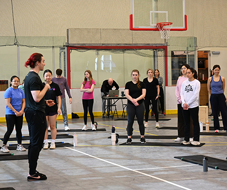 Fitness instructor standing in front of a group of students on basketball court.