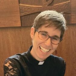 a woman with short brown hair and classes smiles at the camera with her head leaning slightly to the right