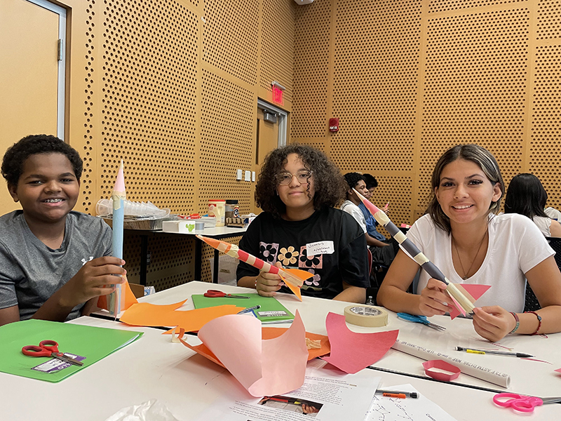 Three students work on building paper rockets