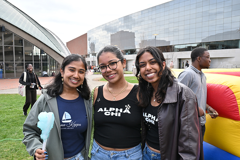 Three students standing outside wearing Alpha Chi tshirts. One is holding blue cotton candy.