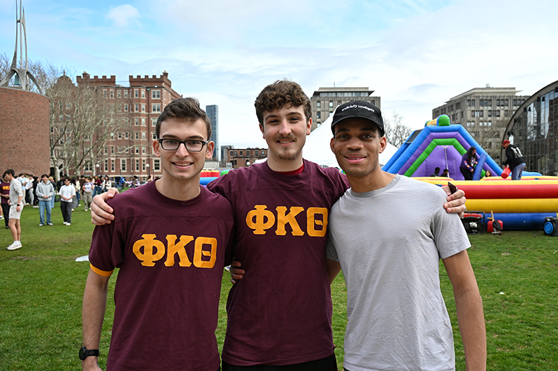 Three students standing in front of a bouncy house at the Greek Carnival