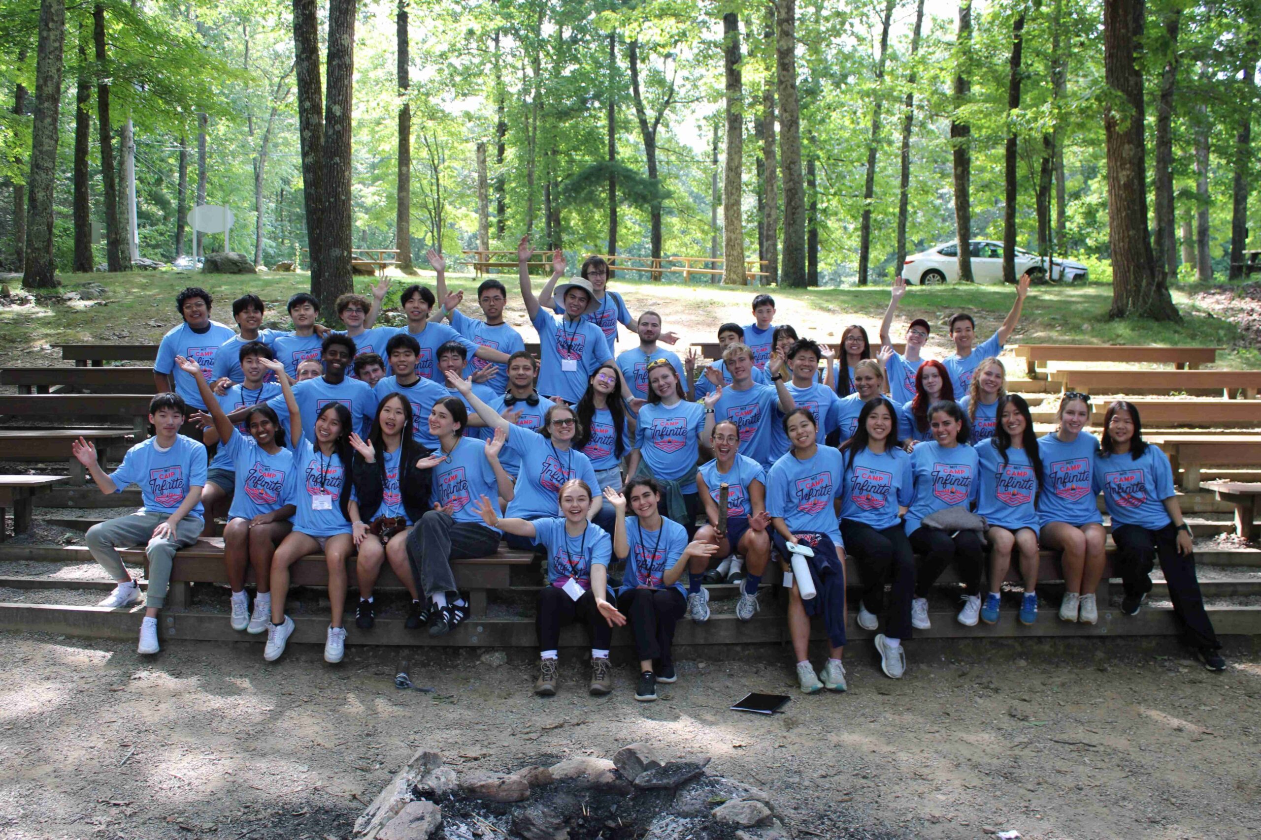 Group of students posing in outdoor amphitheater seats, smiling and raising their hands in the air.