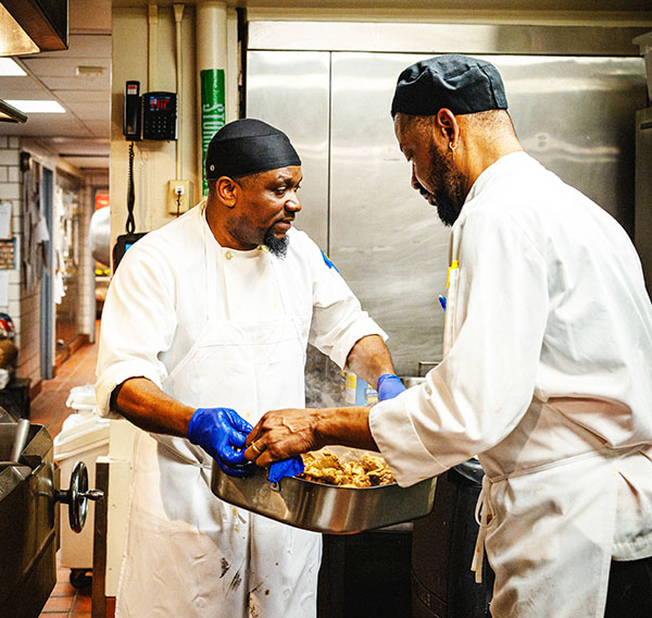 Jean Sauveur passing a pan of food to another chef.